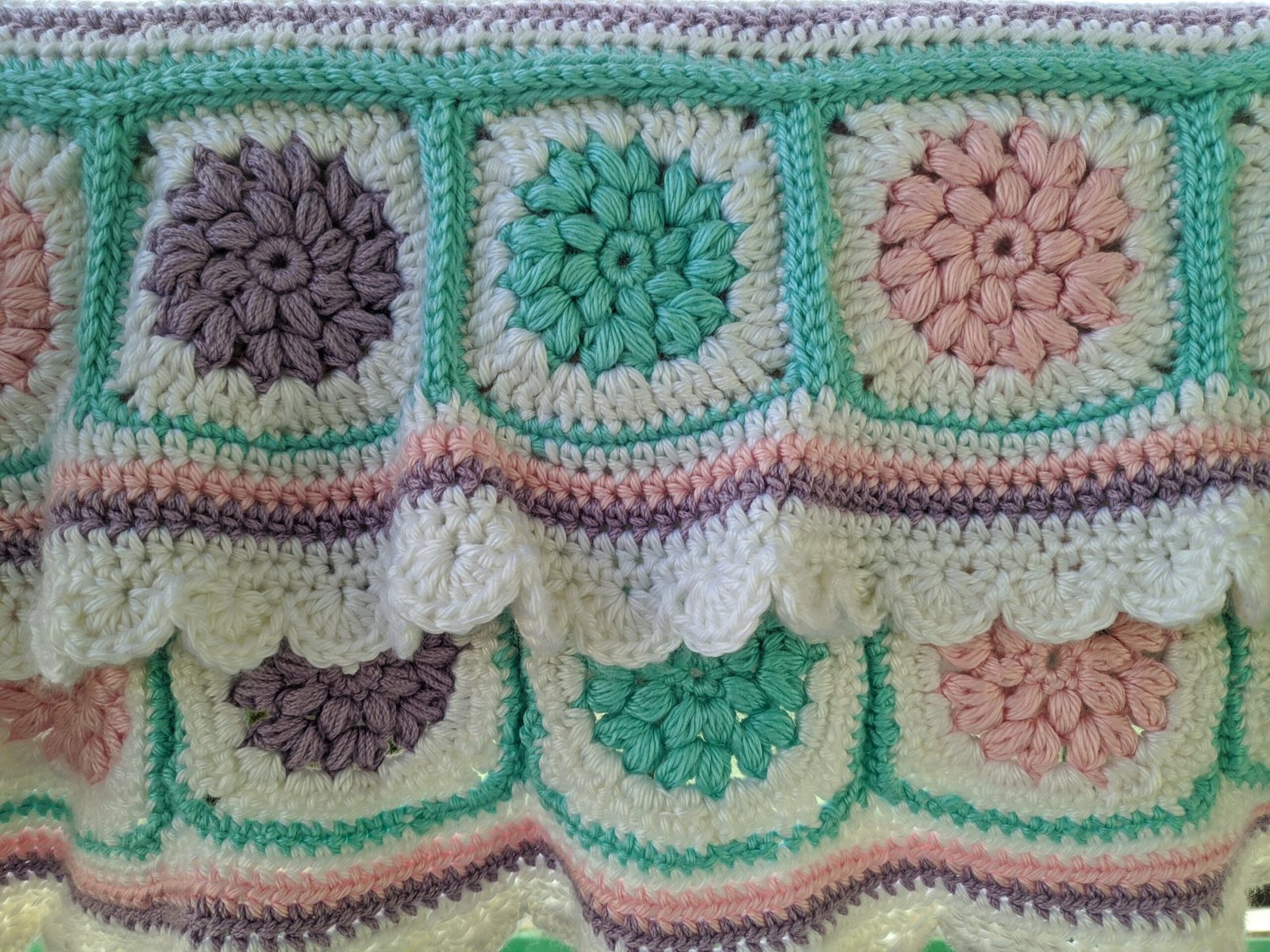A crochet blanket in blue, pink, white and purple stripes
