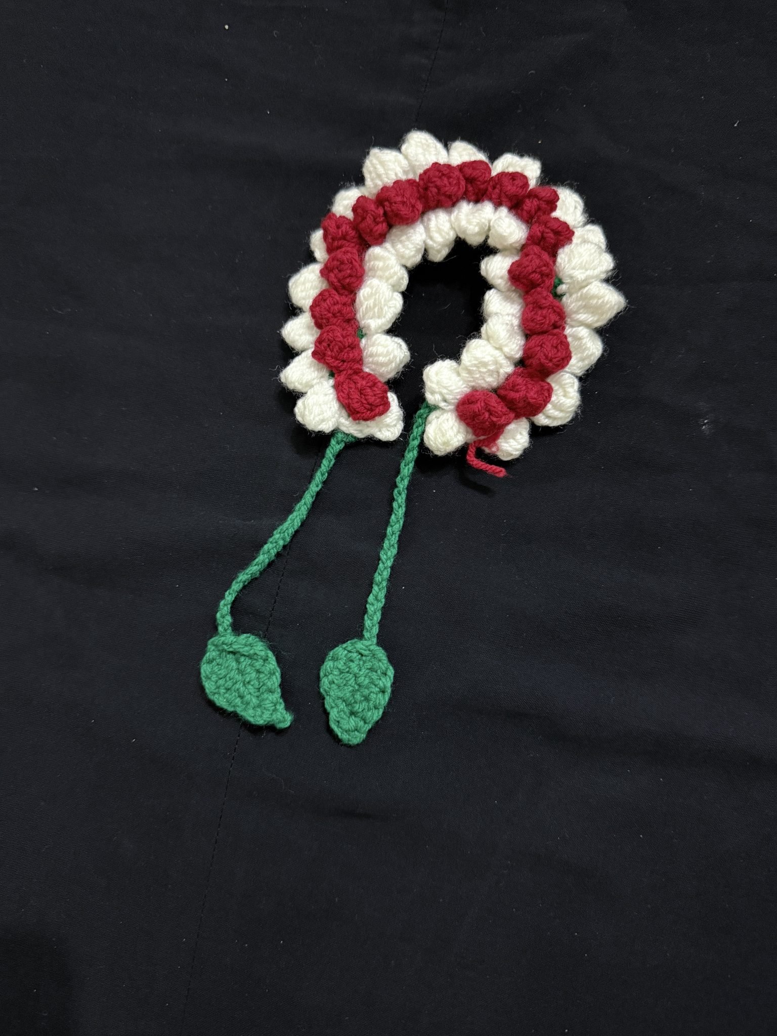 A crocheted garland of red and white flowers with green leaves