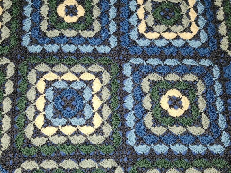 Close-up of a crocheted blanket made from granny squares in green, yellow, blue and dark grey
