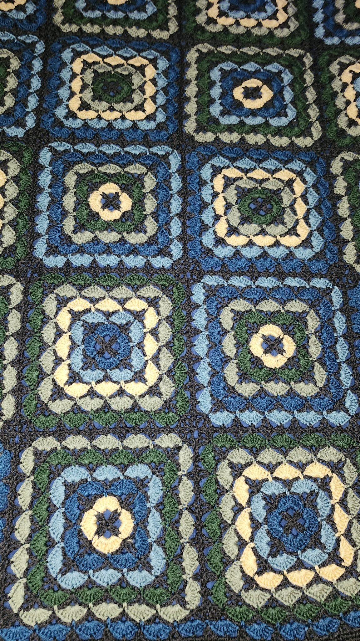 Close-up of a crocheted blanket made from granny squares in green, yellow, blue and dark grey